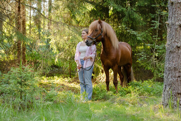 Naklejka premium Woman with Icenlandic horse in forest with sunset on behind