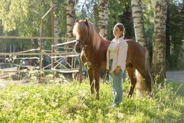 Woman with the Icelandig horse beside the pasture during the sunset