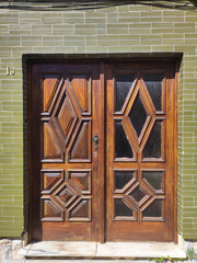 Intricate wooden double doors with geometric patterns on a green tiled wall