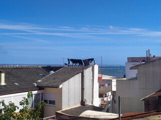 Coastal town rooftops with clothes drying on a line under a clear blue sky, Portugal