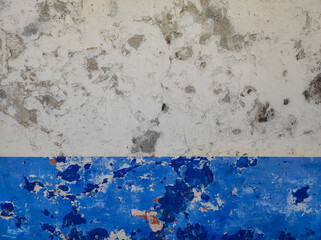Close-up of an old wall with weathered paint and peeling layers. White and blue old wall with peeling paint