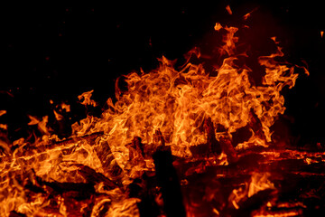 A dramatic image of a fierce fire burning intensely against the dark night sky. The bright orange and yellow flames highlight the raw energy and destructive power of the blaze. Copy space available.