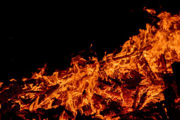 A dramatic image of a fierce fire burning intensely against the dark night sky. The bright orange and yellow flames highlight the raw energy and destructive power of the blaze. Copy space available.