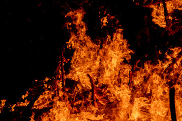 A dramatic image of a fierce fire burning intensely against the dark night sky. The bright orange...