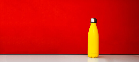 Yellow steel thermo water bootle on red background. Panoramic banner view.