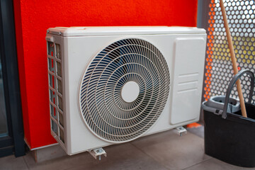 Air conditioner, exterior compressor fixed on red facade.