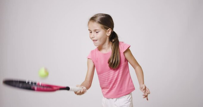 Young female tennis player. Girl in pink sports outfit bouncing a ball.