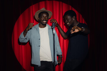 Duet two happy friends African American mans speaking to microphone performing in comedy show open mike stand up on stage with red curtains