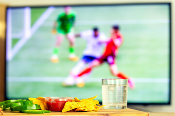 snacks on wooden table against TV screen with football match , football fan concept