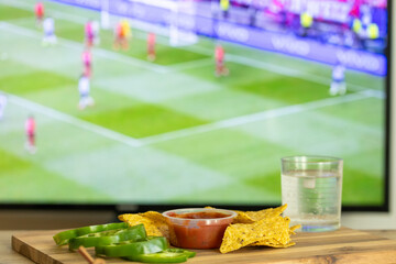 snacks and glass with soda on wooden table against TV screen with football match , football fan concept
