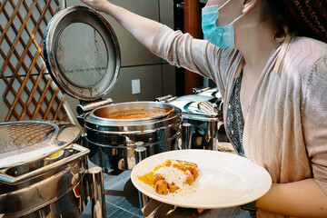 In a hotel setting, a woman is using a food warming machine to fill her plate at the buffet.