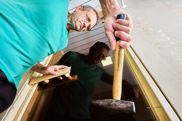 Securing jamb to door frame, nailing wood piece together with hammer.