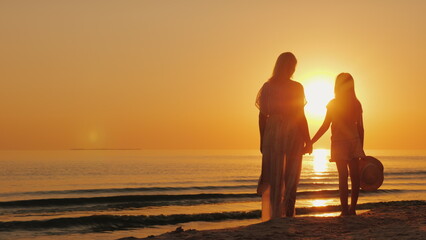 Mom and daughter of seven years together look at the beautiful sunset over the sea. Holiday with a child concept