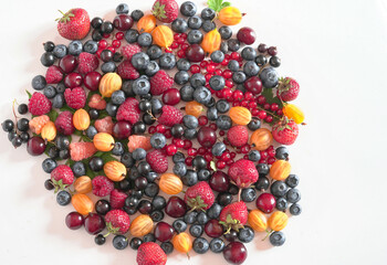 On a white background there are a lot of natural strawberries, raspberries, gooseberries, blueberries, cherries, top view.
