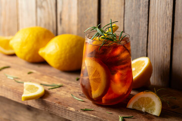 Iced tea or alcoholic cocktail with ice, rosemary and lemon slices on a old wooden table.
