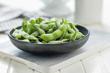 Green edamame pods. Fresh soybeans in plate on white cutting board.