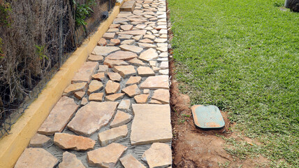 Pathway is being constructed with uneven, natural stone tiles, placed on mesh grid. Two metal...