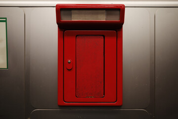 A close-up view of a red metal mailbox mounted on a silver wall.