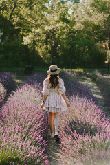 Beautiful young woman, happy girl in a straw hat, summer sundress dress walks in a lavender field...