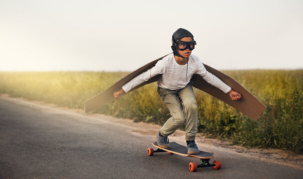 Skateboard, wings and creative kid flying outdoor on road for airplane game, sport and vacation. Pilot, freedom and boy in helmet on street for childhood dream, fantasy and play pretend for adventure - Powered by Adobe
