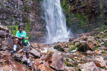Woman stands among the rocks with a water bottle at Sweden's highest waterfall Njupeskär.
