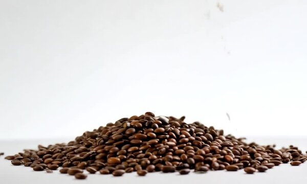 Close-up of coffee beans falling and forming a pile on a white surface, showcasing the details of the beans in motion and the formation of a coffee pile