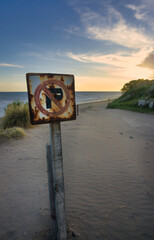 Coastal Scene with Weathered Prohibition Sign Against Ocean Backdrop. Vertical