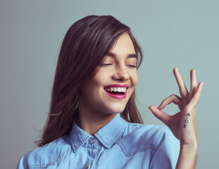 Happy, perfect and woman with hand sign for agreement, opinion or like emoji in studio. Smile, review and gen z girl with okay gesture for approval vote, support or yes icon on grey background