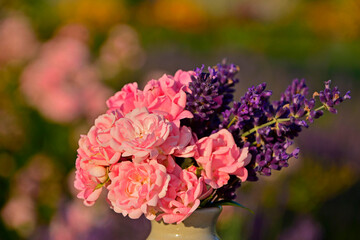 różowe róże i fioletowa lawenda w wazonie na rozmytym tle, róże i lawenda w małym wazonie na tle ogrodu, pink roses and purple lavender in a vase on a blurry background © kateej