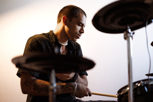Young stylish mixed race musician playing unfocused drums in music studio