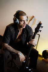 Obraz premium Portrait of stylish guitarist in headphones holding bass guitar in music studio
