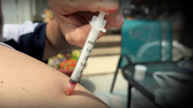 A man injects a B-12 shot into his shoulder at home in the backyard.	