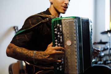 Partial shot of young tattooed musician playing accordion in music studio