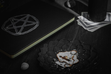 A black metal saucer with burnt paper, a leather book with a magic sign, ritual stones and a candle...