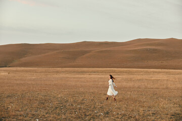 Obraz premium Woman walking through open field with hills in the background and sunlight shining down, travel beauty nature landscape concept