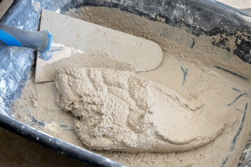 Close-up of freshly mixed mortar with a trowel in a plastic trough.