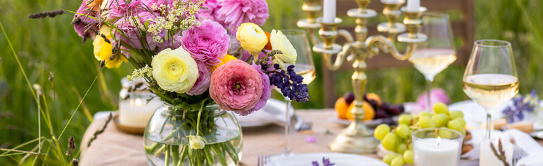 Surprise romantic date outdoors in a meadow. Elegant table with snacks and wine, chandelier with candles as decor. Private party celebration of special event for loving couple. Banner