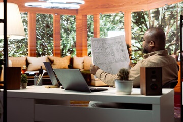 Entrepreneur drafting architectural blueprints and planning an office relocation, focusing on creative workspace interior design and property investment. Evaluating layout of a real estate.