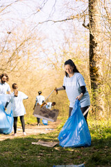 Woman environmentalist grabbing rubbish with a claw tool in the woods, clearing ecosystem of trash...