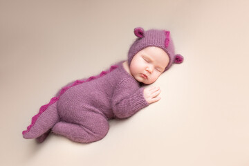 Little adorable newborn baby girl sleeping in a hat with dragon ears. Neutral background. Studio shot of a ten-day-old newborn baby. Beginning of life. Fairy tale. Dragon toy
