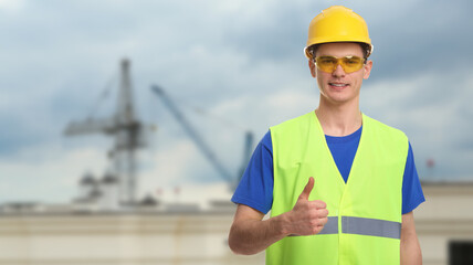 Young man wearing safety equipment and showing thumbs up at construction site. Banner design with space for text