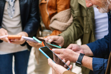 Close up view of senior group of people using mobile phone at city street. Elderly people connected online browsing internet on smart phone device. Technology and elderly lifestyle concept.