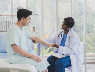 Obraz premium Patient caucasian man with woman nurse carer physical therapist black people two person sitting talk helping support give advice and holding hand arm inside clinic hospital indoor room service.