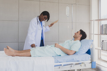 Obraz premium Patient caucasian man lying bed with woman doctor black people stand carer physical therapist two person talk help support and check treat sick person take care of your health in room hospital clinic