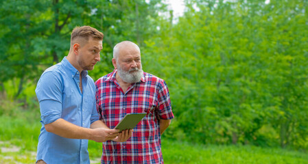 Obraz premium an adult son and an elderly dad are discussing something using a tablet against a background of green nature