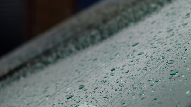 Rain drops on a car windscreen, gathering and running down the slope of the glass