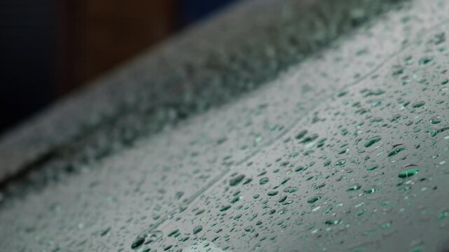 Rain drops on a car windscreen, gathering and running down the slope of the glass