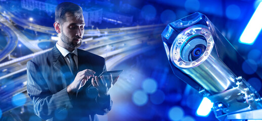 Surveillance camera. Man sets up CCTV equipment. Videocam in vandal-proof housing. Guy controls surveillance camera via e-tablet. CCTV near city road. Surveillance camera near business man