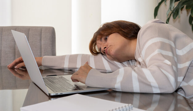 Mujer sentada frente a la computadora recostada sobre su brazo, cansada, aburrida