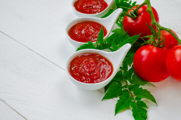 Ketchup and ripe red tomatoes on a white board background. Tomato sauce made from organic farm tomatoes. Homemade ketchup